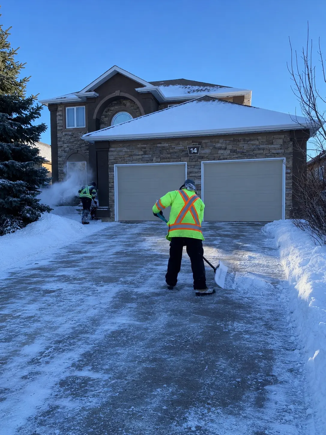 Two Keystone employees finishing a cleared residential driveway on a winter day